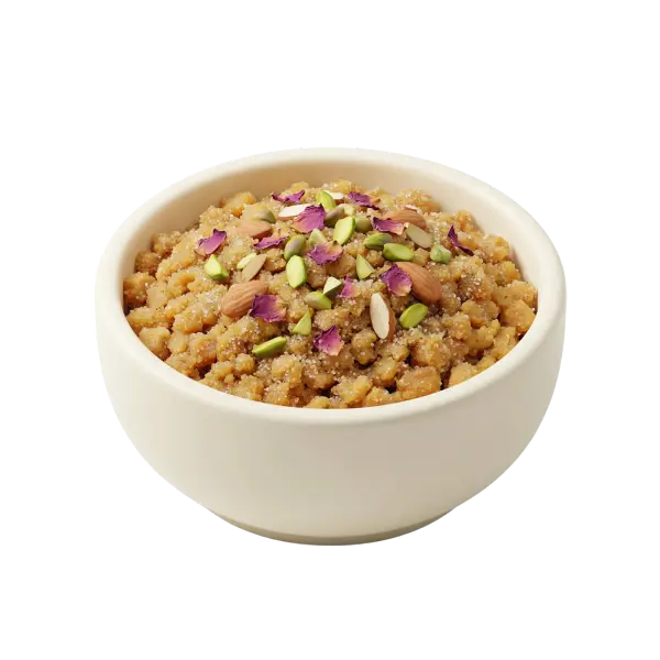 Close-up of a white ceramic bowl filled with crumbly golden semolina-based dessert topped with whole and sliced pistachios, almonds, sugar crystals and dried rose petals, isolated on a black background.