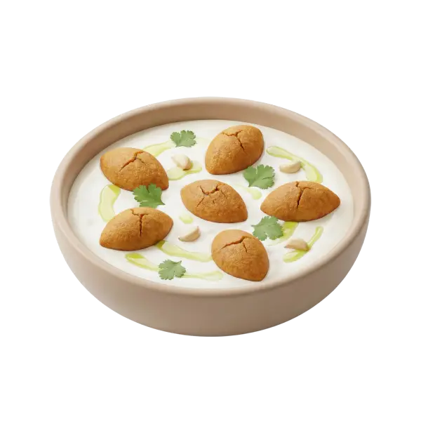 Top-down shot of Kibbeh Labanieh in a shallow beige bowl with seven golden kibbeh dumplings on a creamy white yogurt sauce, garnished with olive oil drizzles, whole garlic cloves and cilantro leaves, isolated on black background.